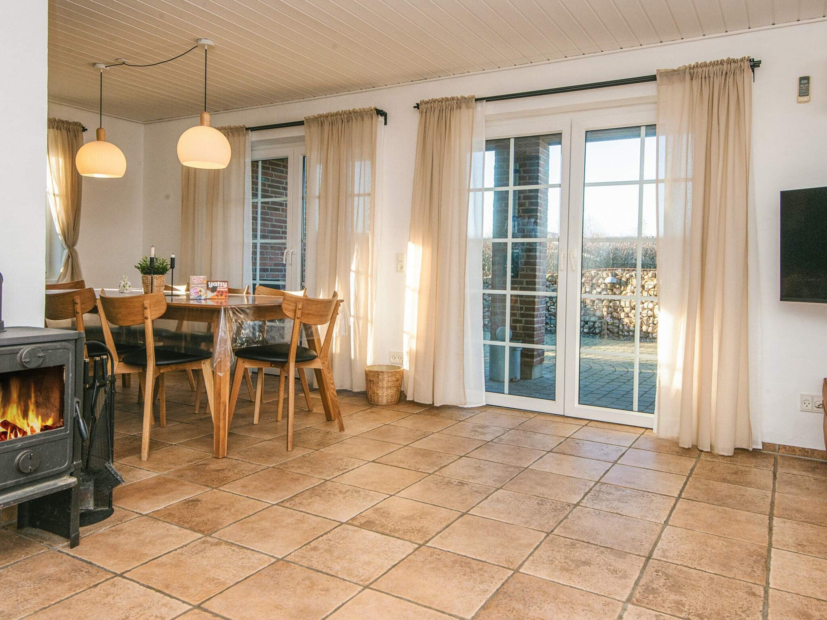Une pièce chaleureuse avec une cheminée, une table à manger avec des chaises, un téléviseur fixé au mur et de grandes fenêtres avec des rideaux.