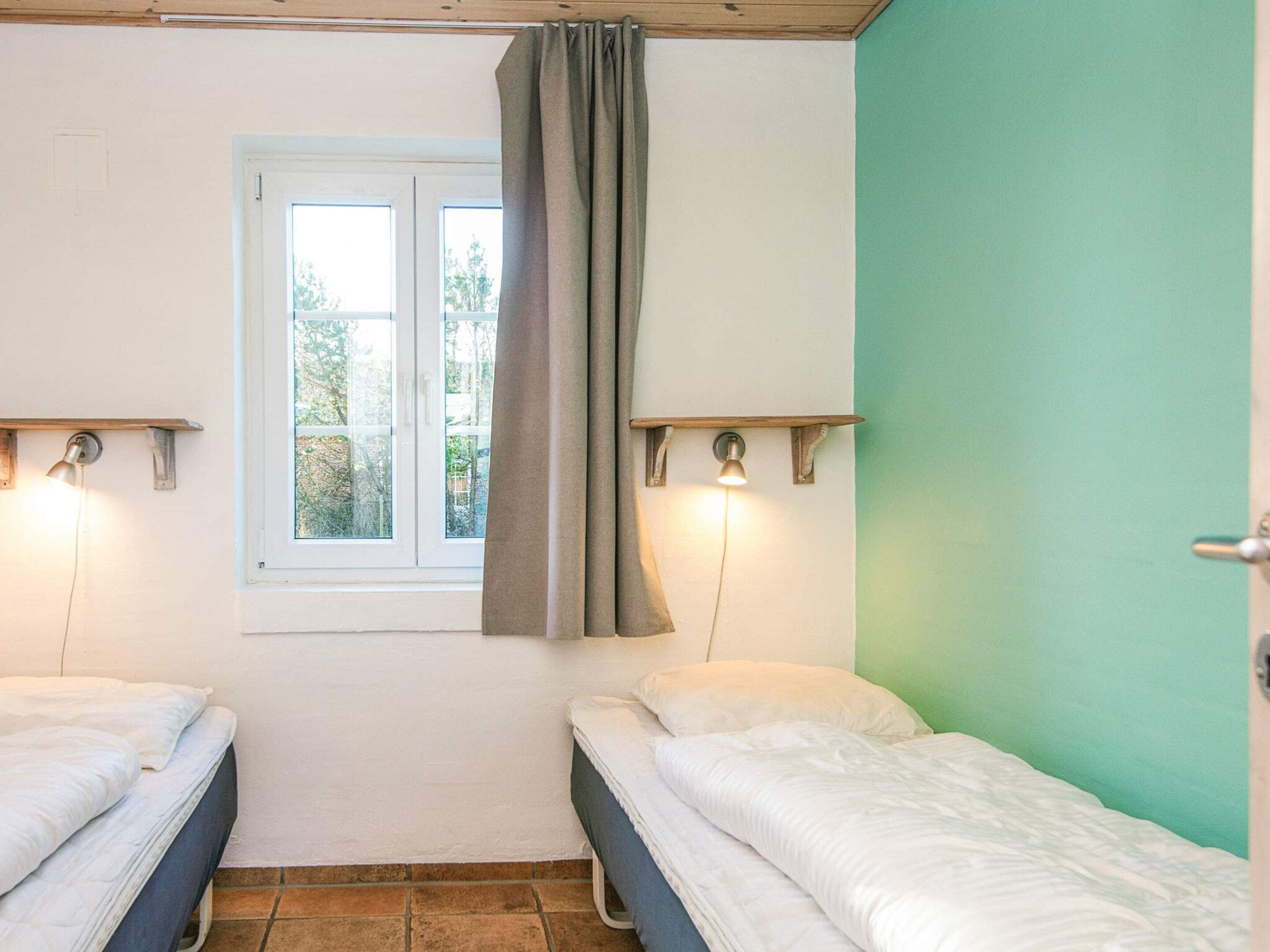 A room with two beds, a window with curtains, and wall-mounted lights.