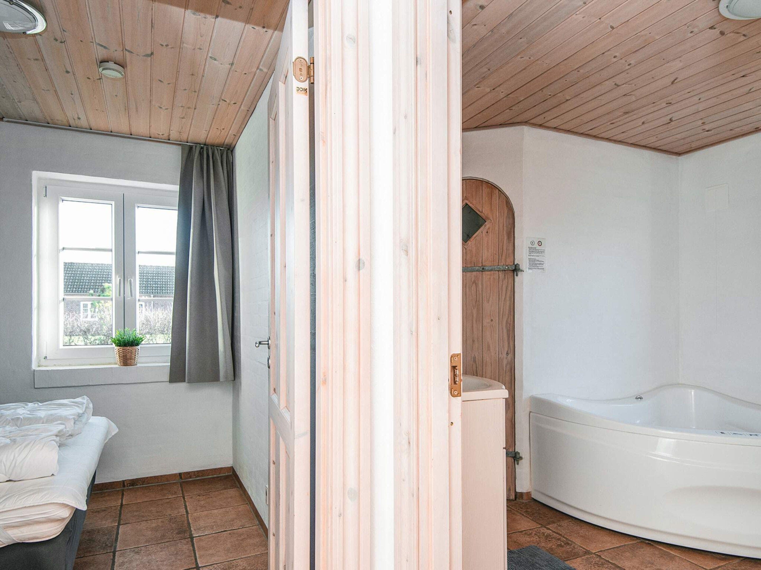 A room with a bed, a window with a view, a wooden door, and a white bathtub.