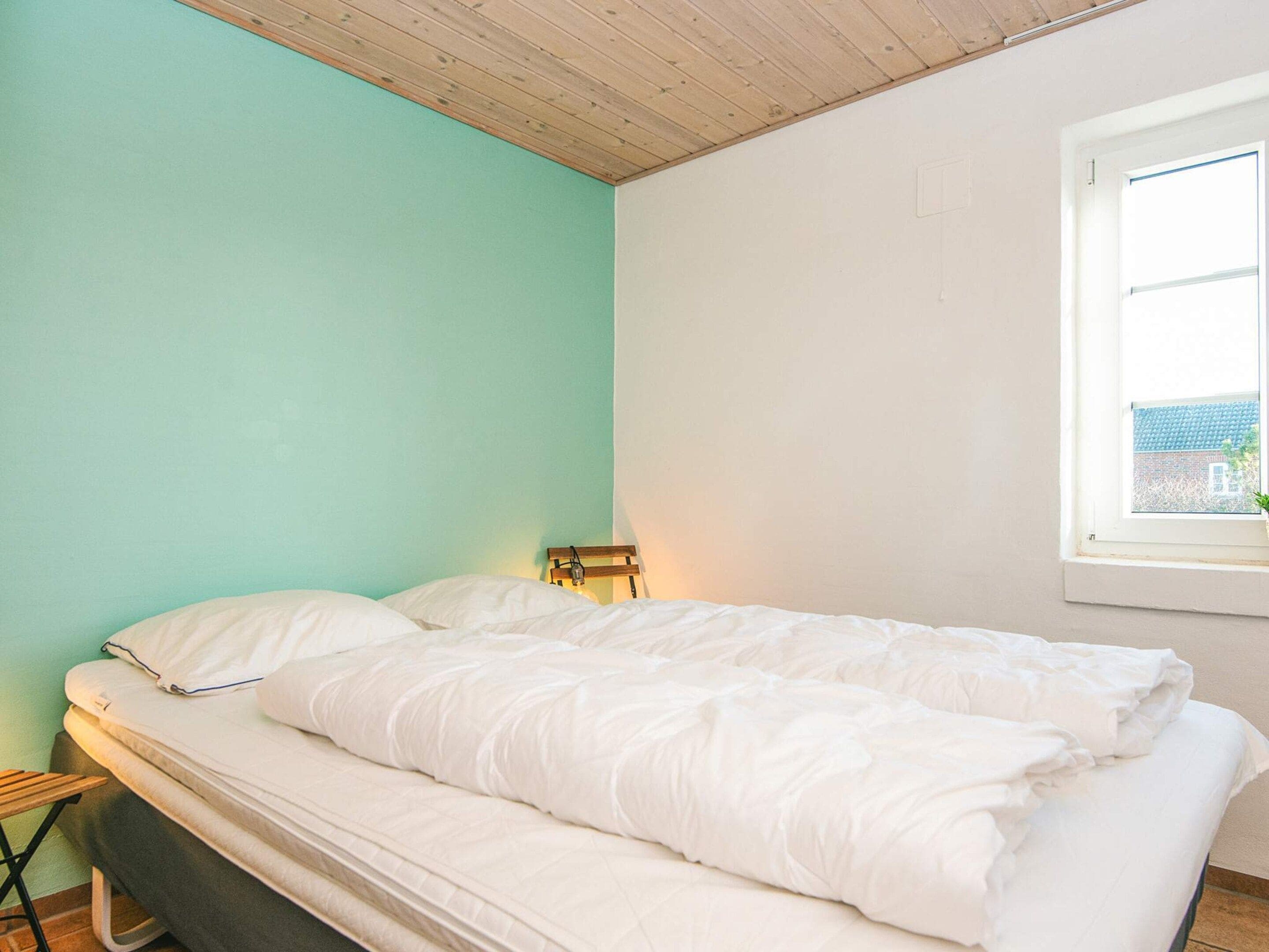 A bedroom with a bed, a window, and a wooden ceiling.