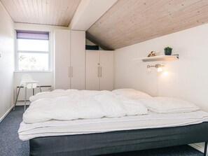A bedroom with a bed, a chair, a wardrobe, and a shelf with a plant.
