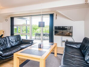 A modern living room with a black leather sofa, a wooden coffee table, and a flat-screen TV mounted on the wall. - 4 Star Holiday Home in Henne (Henne)