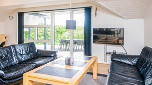 A modern living room with two black leather sofas, a wooden coffee table, and a flat-screen TV mounted on the wall.