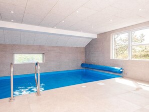 A modern indoor swimming pool with a clear ceiling, a window, and a blue pool liner.