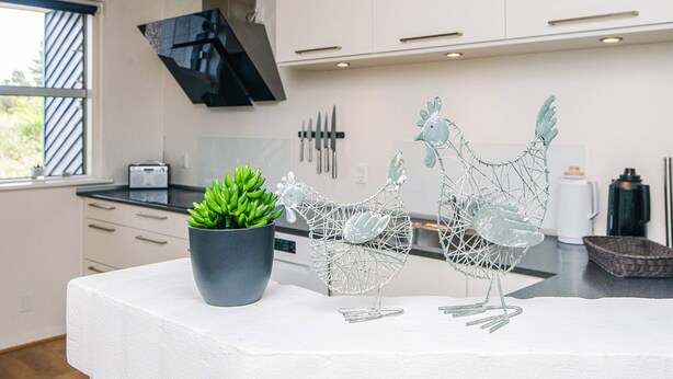 A modern kitchen with white cabinets, a black range hood, and decorative metal chickens on the counter.