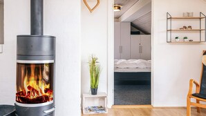 A modern living room with a wood-burning stove, a small plant, a bookshelf, and a bed in the background.