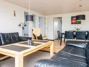 A modern living room with a sofa, a coffee table, and a dining area with chairs and a table. - 4 Star Holiday Home in Henne (Henne)
