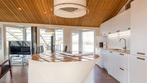 Uma cozinha moderna com armários brancos, uma ilha central e um espaço de refeições com televisão e cadeiras.