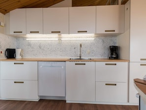 A modern kitchen with white cabinetry, a dishwasher, a coffee maker, and a speckled backsplash.