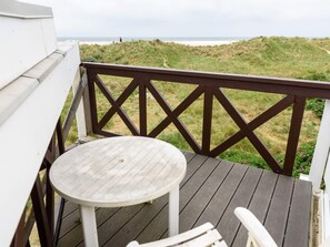 Una terraza de madera con una mesa redonda y sillas, con vistas a una playa con dunas.