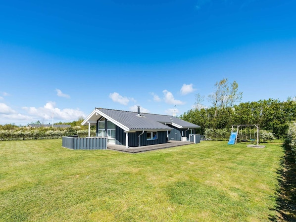 A modern house with a large lawn, a swing set, and a satellite dish.