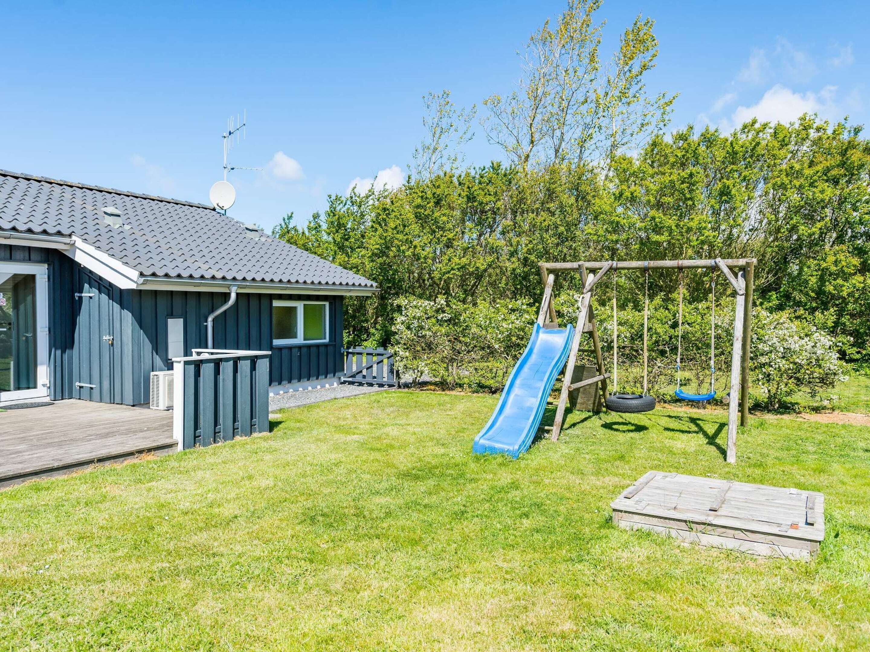 Uma casa com fachada azul, um deck de madeira, um escorrega azul e um baloiço.