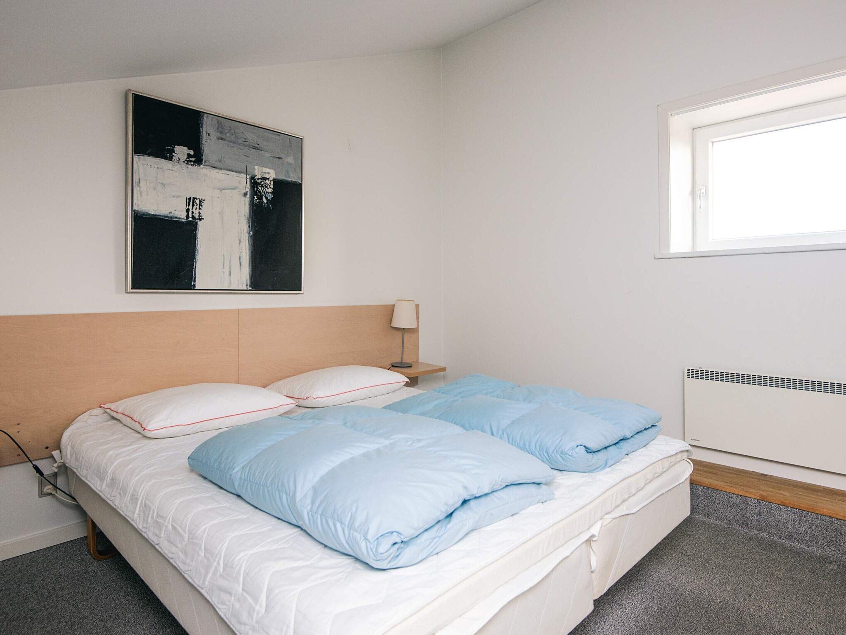 Un dormitorio con cama, mesita de noche, lámpara, radiador y ventana.
