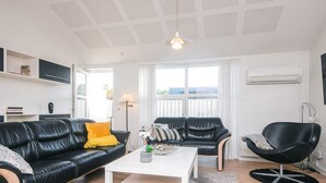 Ein modernes Wohnzimmer mit einer schwarzen Ledersofa, einem weißen Couchtisch und einem schwarzen Sessel. Es gibt ein Fenster mit Vorhängen, eine Stehlampe und eine Deckenleuchte.