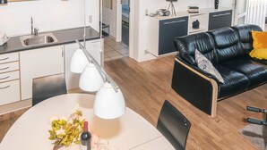 Eine moderne Küche mit weißen Schränken, einem Esstisch mit Blumenvase und einem schwarzen Ledersofa mit gelbem Kissen.