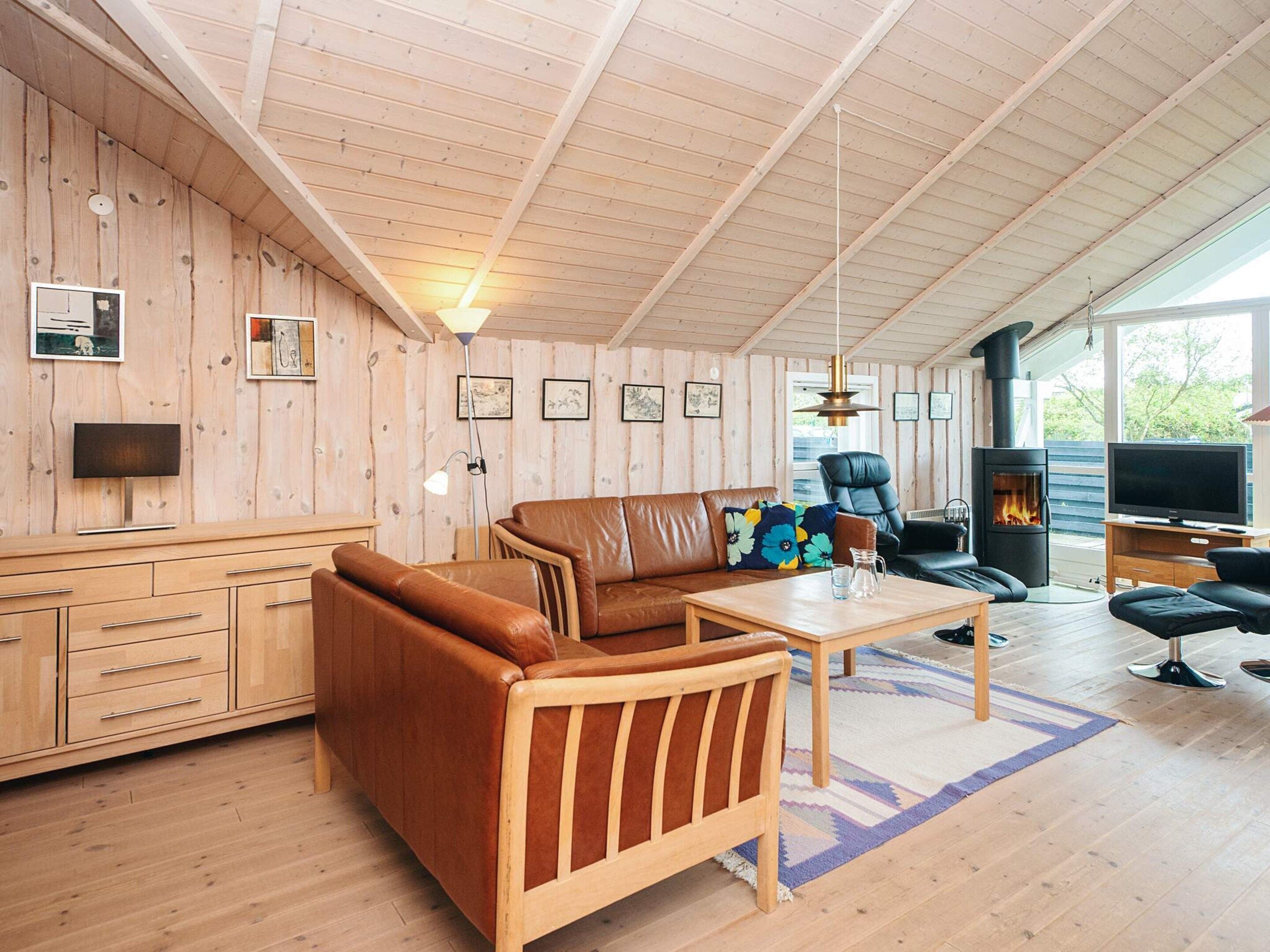 L’intérieur d’un chalet accueillant, avec un plafond en bois, un canapé, une table, un téléviseur et une cheminée.