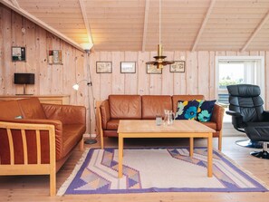 A cozy living room with a wooden ceiling, a brown leather sofa, a wooden coffee table, and a black chair.