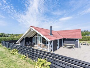 Ett modernt hus med ett rött tak, stora fönster och en uteplats.