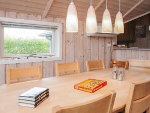 A wooden dining table with chairs, a window with a view of greenery, and a chessboard.