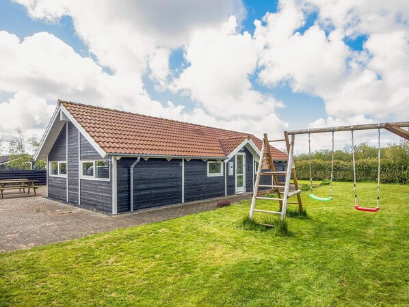 A house with a tiled roof, a wooden swing set, and a paved patio area.