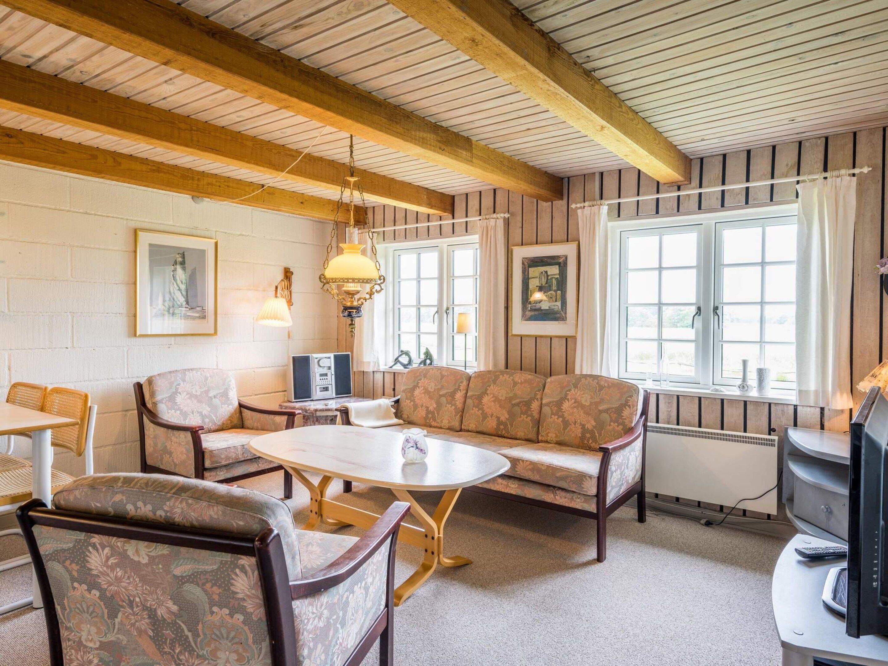 A cozy room with a wooden ceiling, a sofa, chairs, a table, and a television.