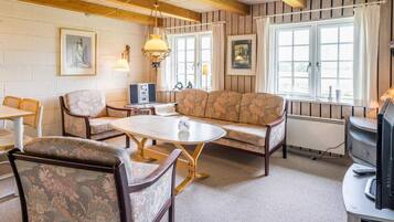 A cozy room with a wooden ceiling, a sofa, chairs, a table, and a television.