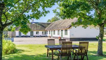 A rustic thatched-roof building with a gravel courtyard and wooden furniture.