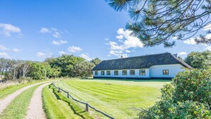 A white building with a thatched roof, surrounded by a well-maintained lawn and a gravel path. - 4 Person Holiday Home in Norre Nebel (Norre Nebel)