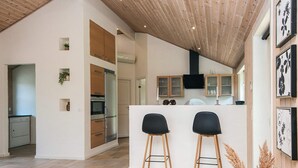 Una cocina moderna con una isla central, armarios de madera y un horno empotrado. Hay dos taburetes negros frente a la isla.