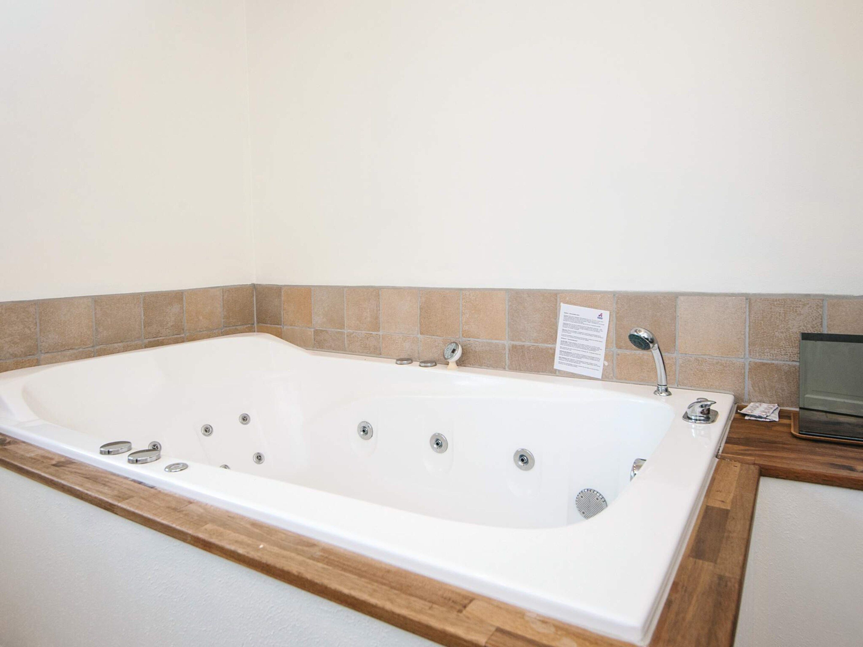 Une grande baignoire blanche dotée de plusieurs robinets et d’un bord en bois.