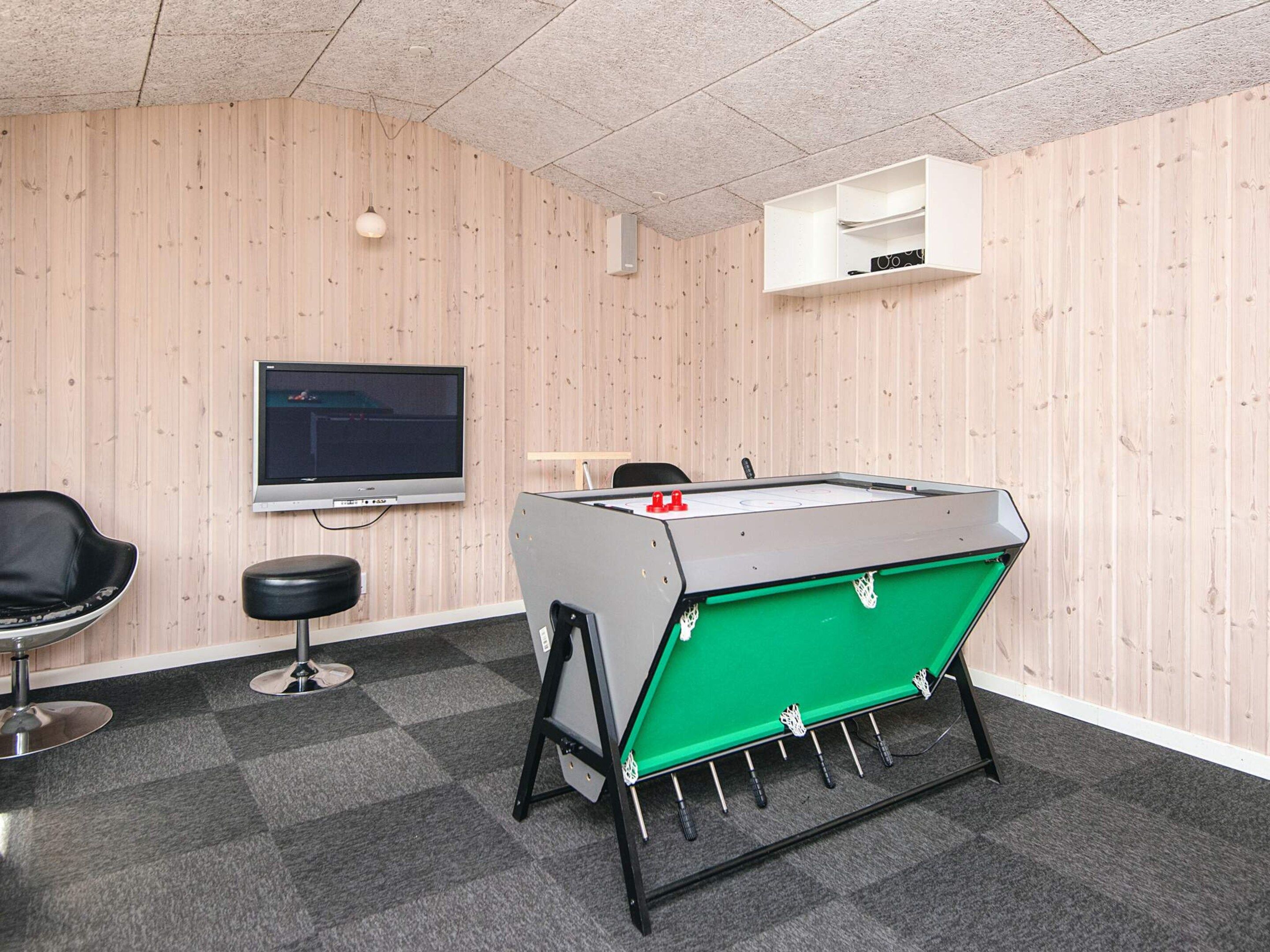 A room with a foosball table, a television, a chair, and a small shelf.