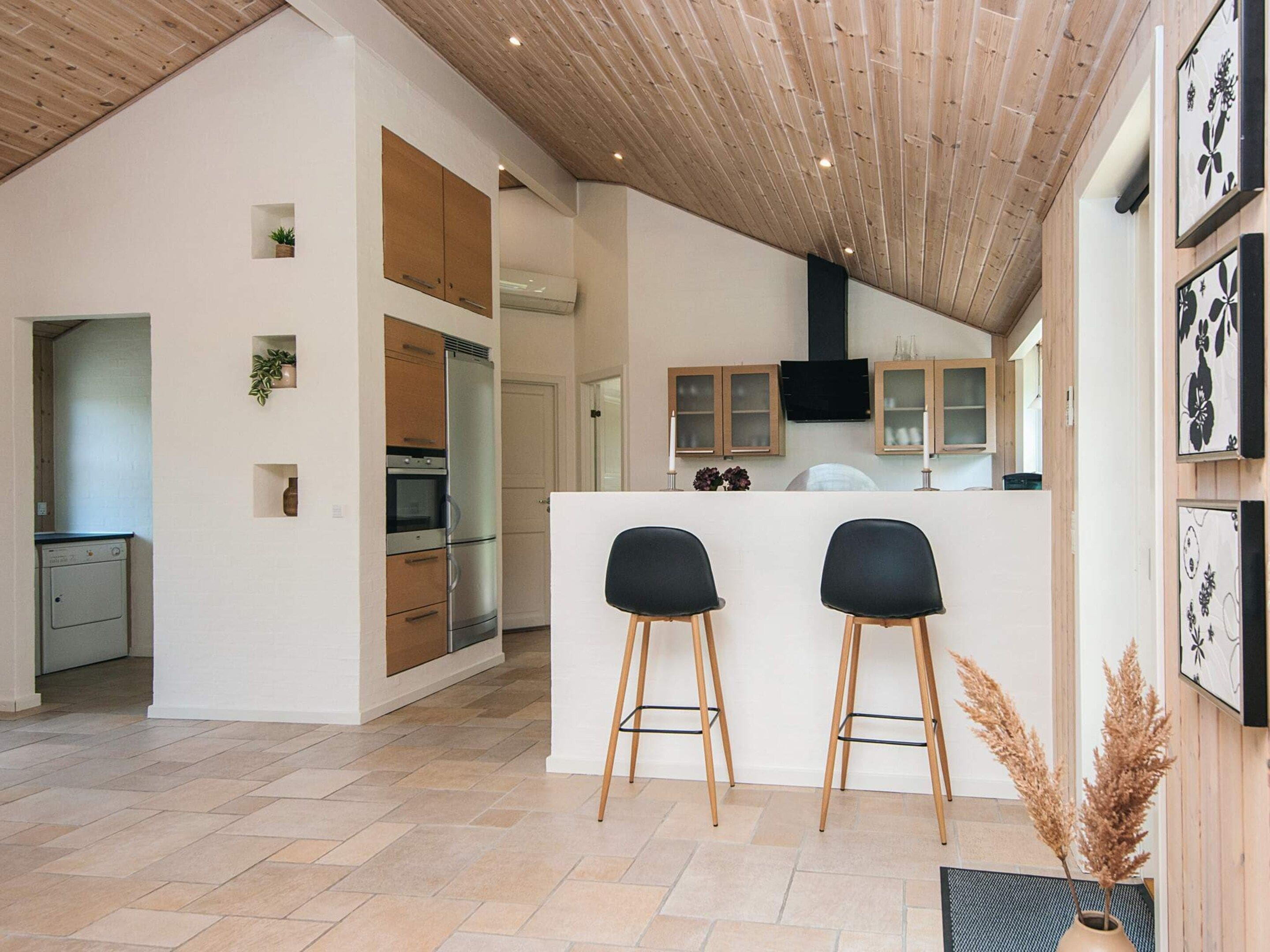 A modern kitchen with a central island, wooden cabinets, and a built-in oven. There are two black bar stools in front of the island.