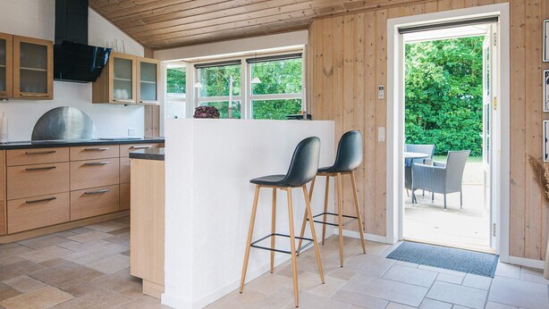 Una cocina moderna con armarios de madera, una isla central y un comedor con mobiliario de exterior.