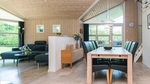 Una cocina moderna con techo de madera, un comedor con mesa y sillas de madera, y una zona de estar con sofá y mesa de centro.
