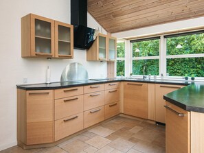 A modern kitchen with wooden cabinets, a stainless steel range hood, and a large window with a view of greenery.