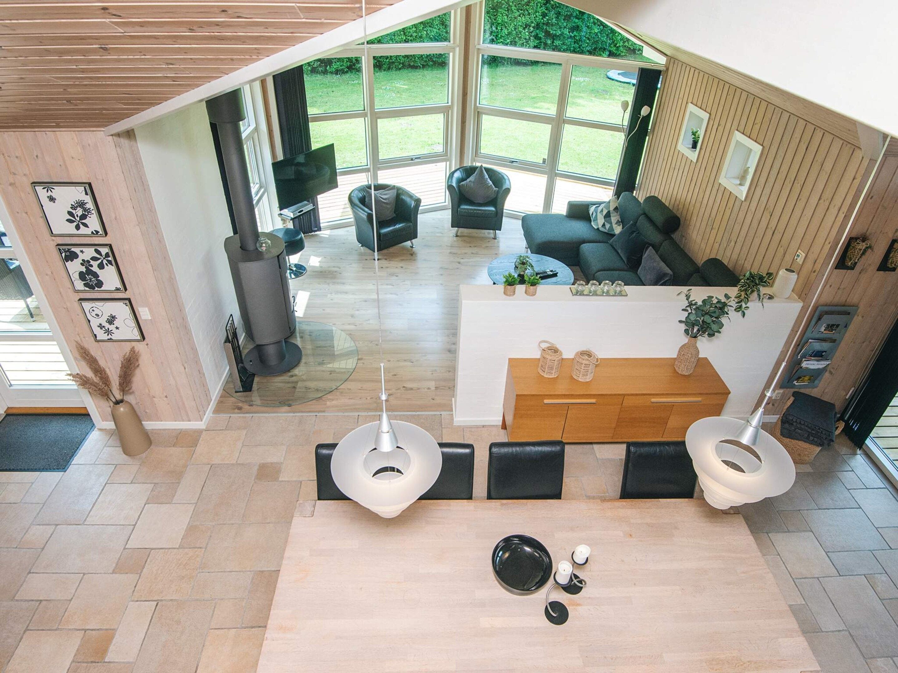 Ein modernes Interieur mit Holzbalkendecke, einem Essbereich mit zentralem Tisch und einer Sitzecke mit Sofas und Fernseher.
