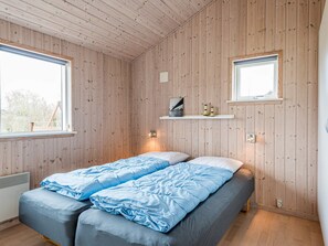 A room with wooden walls, a bed with blue bedding, a window, and a shelf with decorative items. - 5 Star Holiday Home in Tarm (Tarm)