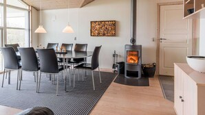 Una cocina moderna con estufa de leña, comedor con sillas y mesa, y un amplio ventanal que proporciona luz natural.