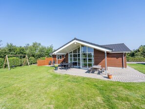 A modern house with a covered patio, a swing set, and a brick patio.