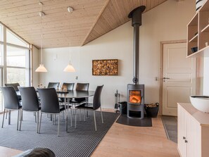 A modern interior with a round dining table, black chairs, a wood-burning stove, and a large window.