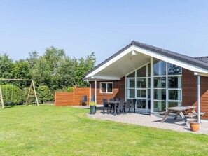 A modern house with a covered patio, a swing set, and a wooden fence. - 5 Star Holiday Home in Tarm (Tarm)