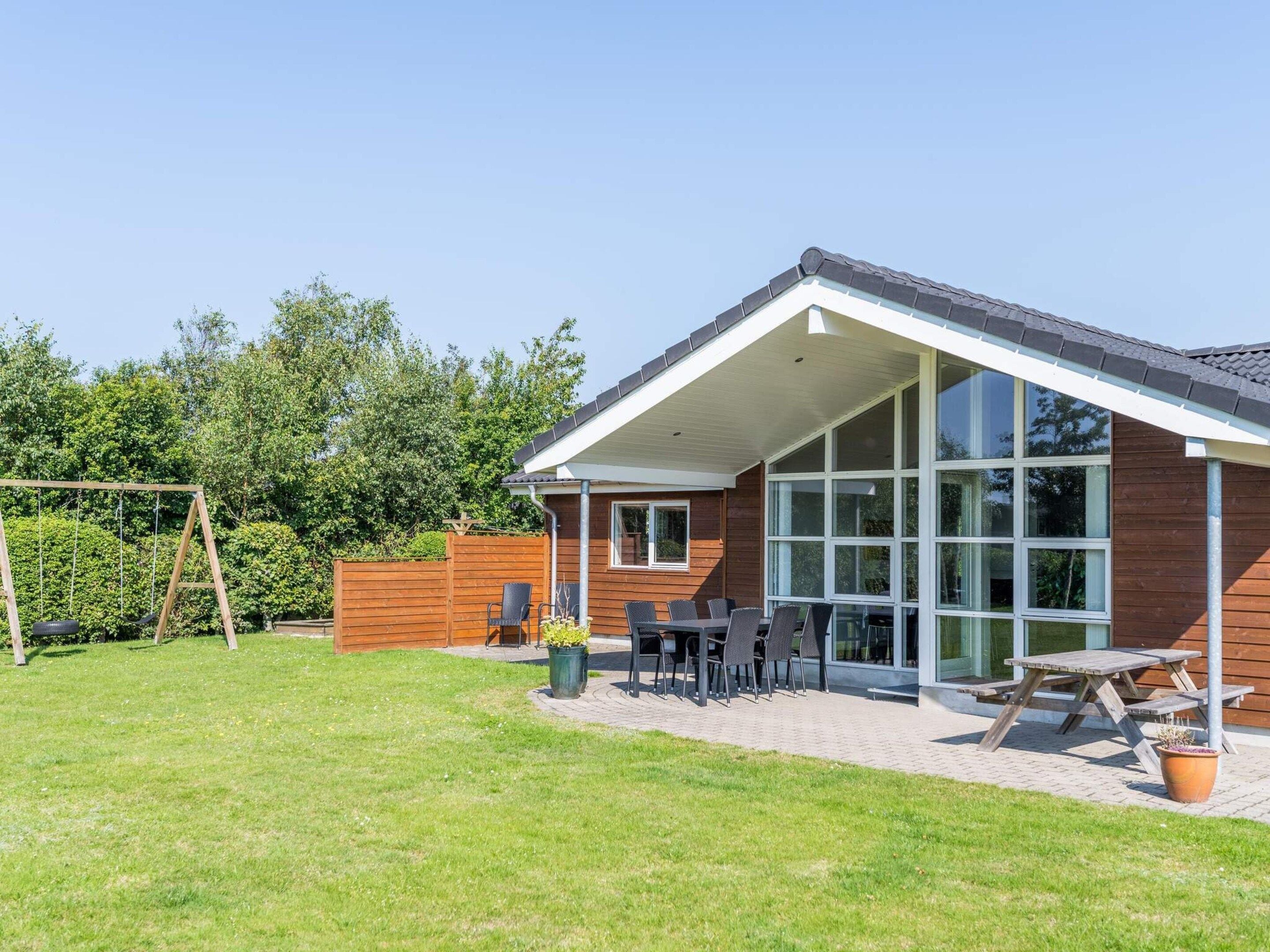 A modern house with a patio, large windows, and a swing set.