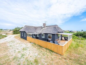 A thatched-roof house with a wooden deck and a glass enclosure. - Bright Seaside Retreat in Haurvig-by Traum (Hvide Sande)