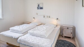 Un lit double avec une literie blanche, une table de chevet, une petite armoire, une étagère murale agrémentée d’objets décoratifs et un tapis rond sur le sol.