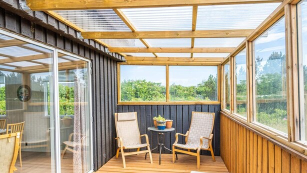 Une véranda avec des poutres en bois, de grandes fenêtres et une vue sur la verdure.