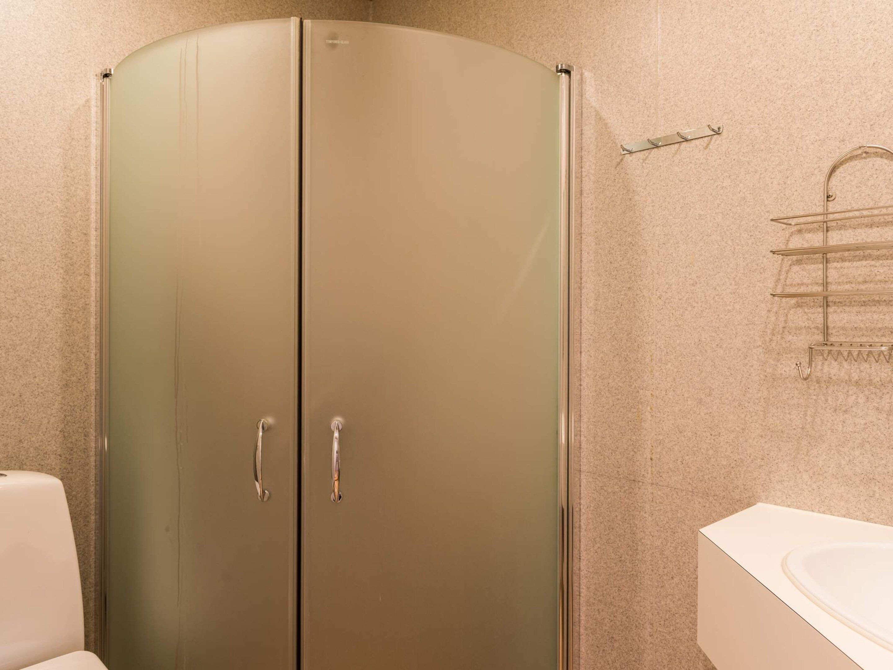 A bathroom with a double door shower, a towel rack, and a toilet.