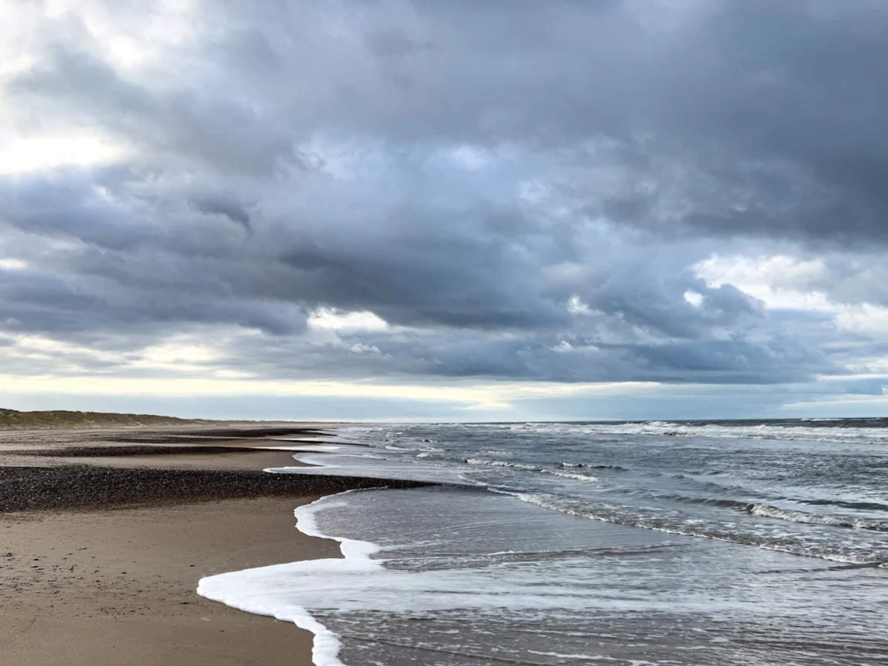 A beach with waves approaching the shore under a cloudy sky.