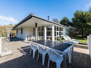 Ein überdachter Patio-Bereich mit Tisch und Stühlen, einer Pergola und Blick auf ein Haus mit großen Fenstern.