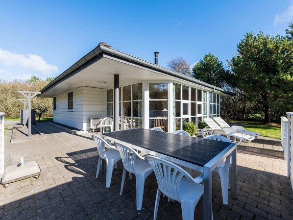 A covered patio with a table and chairs, a pergola, and a view of a house with large windows.