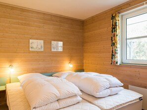 A room with wooden walls, a bed with white bedding, two wall-mounted lights, and a window with curtains. - 4 Star Holiday Home in Norre Nebel (Norre Nebel)